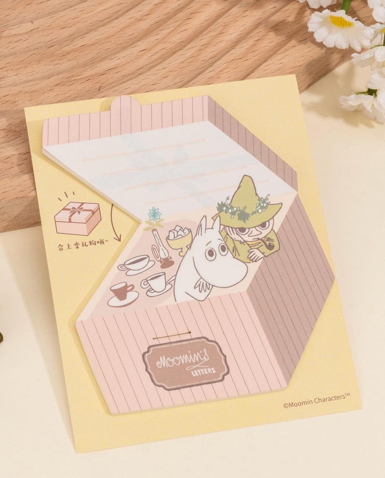 May include: A yellow notepad with a pink and brown striped design. The notepad features illustrations of Moomin characters and the text "Moomin's Letters". The notepad has a gift box illustration and text in Chinese.