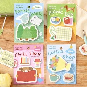 May include: Four colorful sticky note pads with themed illustrations. The themes include "Forest Walk," "Picnic Day," "Chill Time," and "Coffee Shop." Each pad features unique designs like trees, a dog, a book, and a coffee cup. The pads are rectangular with rounded corners.