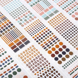 Puede incluir: Varias hojas de pegatinas adhesivas con una variedad de formas, incluyendo círculos, cuadrados y rectángulos. La colección incluye secuencias numéricas, el alfabeto en letras mayúsculas y bloques de colores sólidos en tonos naranja, azul y verde.
