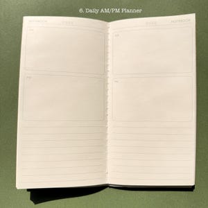 May include: An open daily AM/PM planner notebook with white pages. The top of each page is labeled NOTEBOOK and includes a date field. Each page features two large rectangular boxes labeled AM and PM, followed by several horizontal lines.