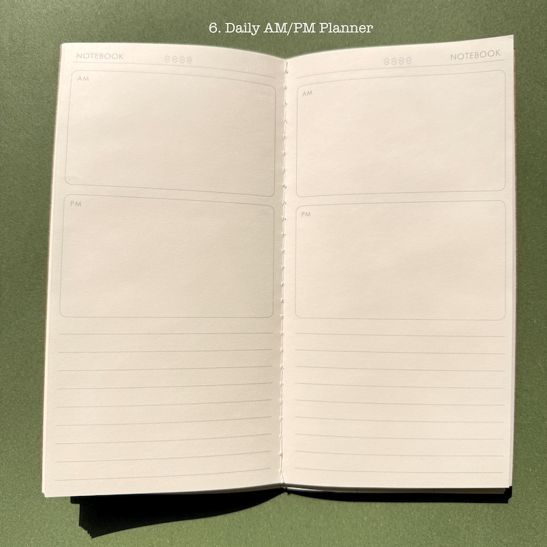 May include: An open daily AM/PM planner notebook with white pages. The top of each page is labeled NOTEBOOK and includes a date field. Each page features two large rectangular boxes labeled AM and PM, followed by several horizontal lines.
