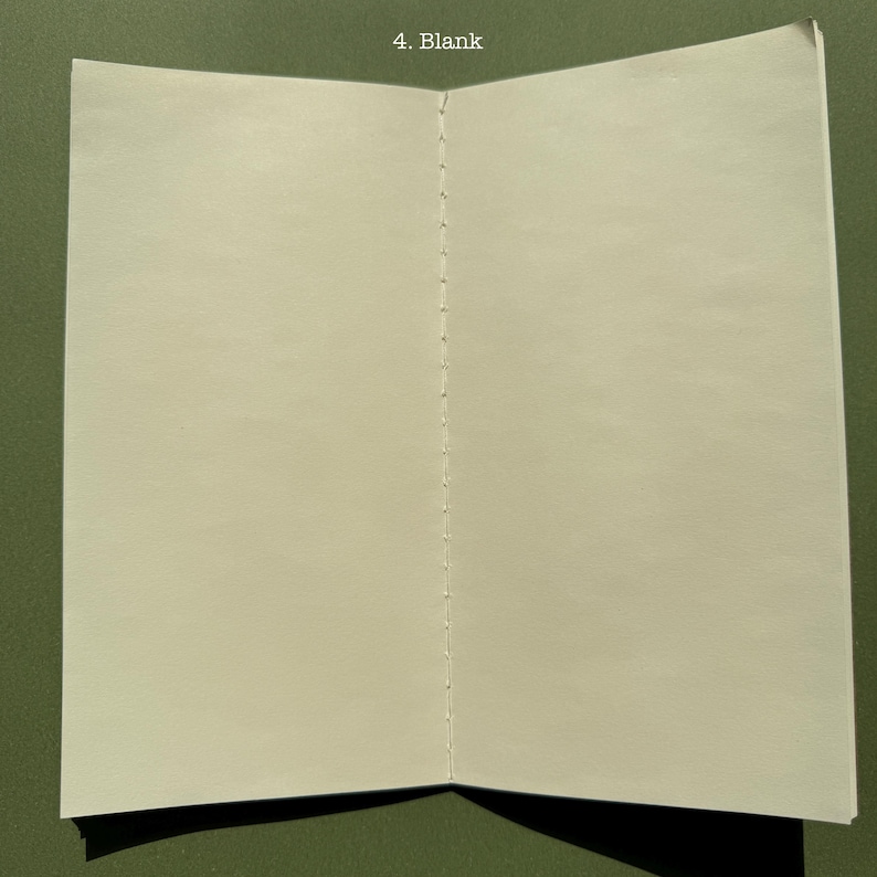 May include: An open notebook with cream-colored, blank pages featuring a visible white thread spine binding down the center. The text '4. Blank' is printed in white at the top center of the page spread, showcasing a simple, functional design.