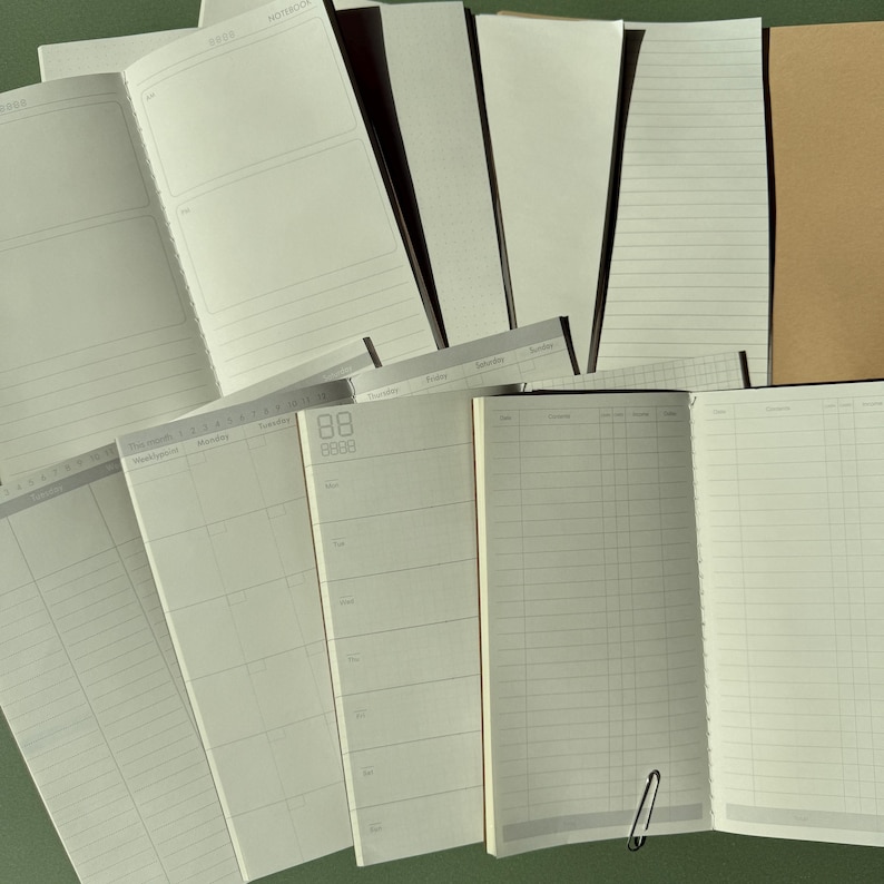 May include: A collection of open notebooks and planners featuring various page layouts including lined, grid, and calendar formats. The pages are off-white with thin gray lines and text, and one notebook includes a small silver metal paper clip.