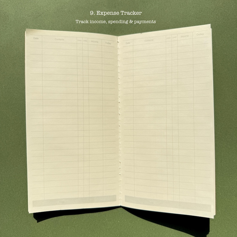 May include: An open expense tracker notebook with off-white pages featuring printed grids for tracking income, spending, and payments. The text 9. Expense Tracker and Track income, spending & payments is printed at the top of the page.
