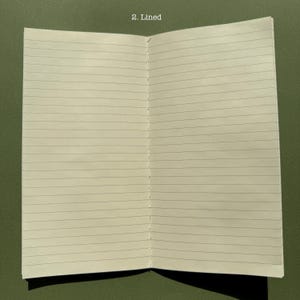 May include: An open notebook with off-white pages featuring horizontal black lines. The center fold shows visible white thread stitching binding the pages together. The text 2. Lined is printed in white at the top center of the page spread.