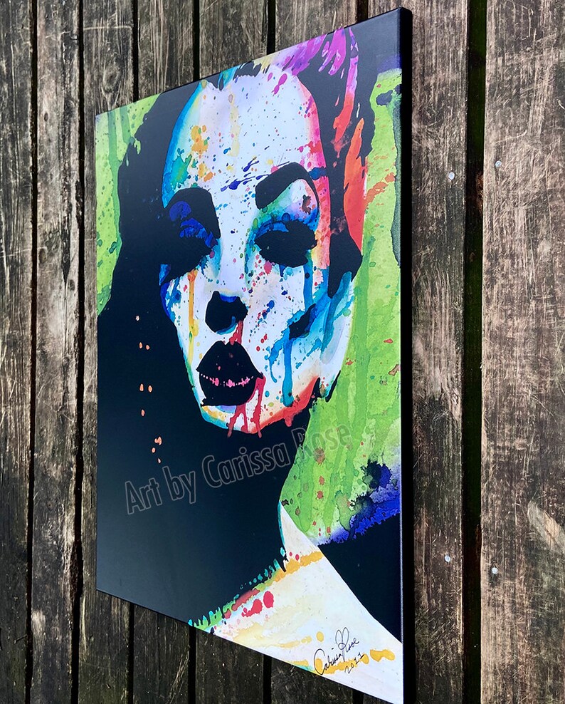 May include: A colorful abstract portrait print featuring a woman's face with vibrant watercolor paint splatters. The artwork includes the text "Art by Carissa Rose" and a signature. The color palette includes black, white, blue, red, and green.