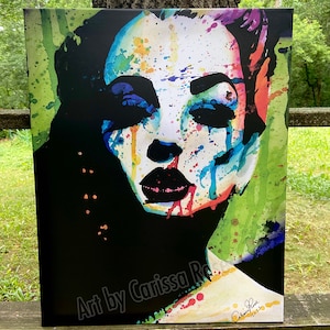 May include: A canvas print featuring a colorful abstract portrait of a woman's face. The artwork uses a vibrant palette of blues, greens, reds, and yellows against a black background. The artist's signature and the year 2022 are visible.
