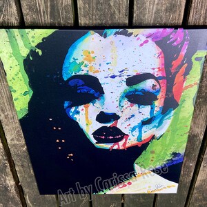 May include: A colorful pop art portrait of a woman with vibrant splashes of blue, red, and yellow paint. The artwork features bold black accents and the text "Art by Carissa Rose".