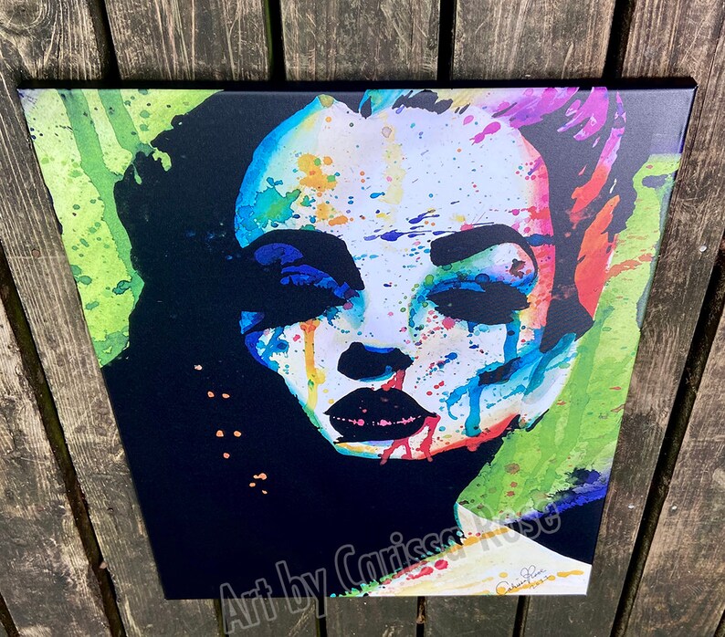 May include: A colorful pop art portrait of a woman with vibrant splashes of blue, red, and yellow paint. The artwork features bold black accents and the text "Art by Carissa Rose".
