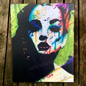 May include: A canvas print featuring a colorful abstract portrait of a woman's face. The artwork uses a vibrant palette of blues, reds, greens, and yellows, with black accents. The artist's signature and the year 2022 are visible.