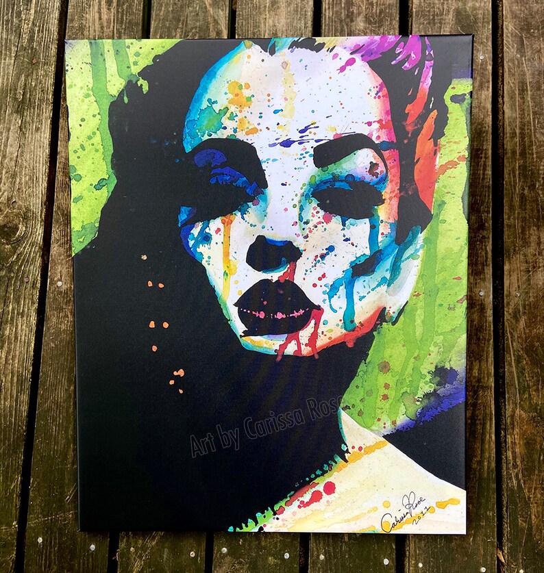 May include: A canvas print featuring a colorful abstract portrait of a woman's face. The artwork uses a vibrant palette of blues, reds, greens, and yellows, with black accents. The artist's signature and the year 2022 are visible.