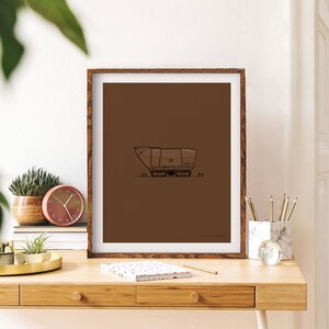 Op de afbeelding: Een ingelijst afdruk van een bruine en zwarte lijntekening van een ruimteschip op een bruine achtergrond.