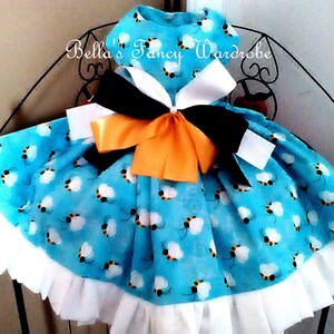 May include: A blue and white dress with a bee pattern and a large orange and black bow. The dress has a white ruffle trim.