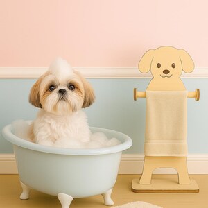 May include: A small dog sits in a light blue bathtub filled with bubbles. A wooden dog-shaped towel rack holds a beige towel. A matching beige bath mat sits on the floor. The background is a pastel pink and blue.