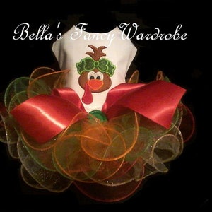 May include: A white pet outfit with a turkey graphic, a red bow, and layers of orange, green, and gold tulle. The text "Bella's Fancy Wardrobe" is arched above the outfit.