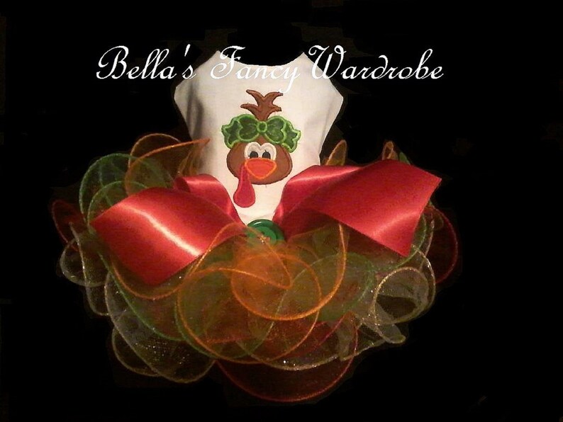 May include: A white pet outfit with a turkey graphic, a red bow, and layers of orange, green, and gold tulle. The text "Bella's Fancy Wardrobe" is arched above the outfit.