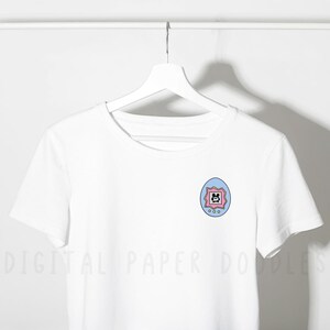 May include: A white short-sleeved t-shirt featuring a small graphic on the left chest. The graphic is a light blue and pink egg-shaped digital pet device with a screen displaying a black pixelated character and three small circular buttons below.