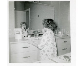 Joven admirando su reflejo en un espejo de tocador mientras se pone lápiz labial, foto vintage