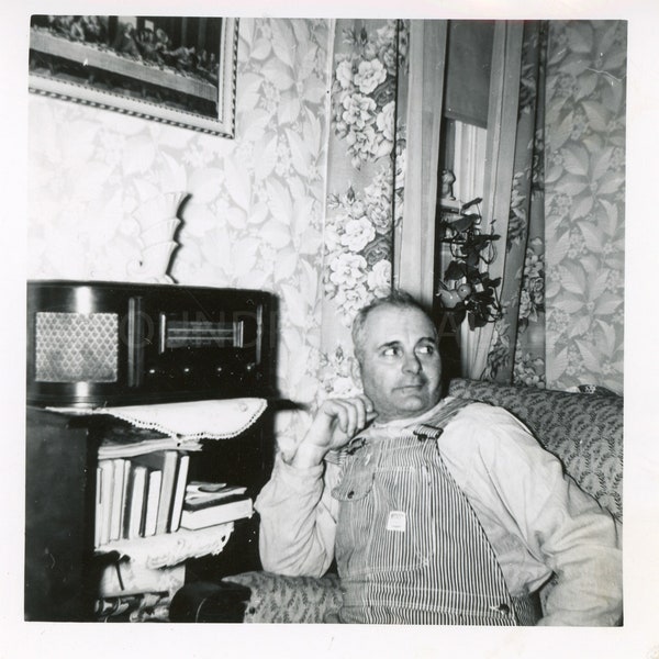 Un cheminot costaud en salopette assis dans son fauteuil préféré près de sa radio vintage dans un salon confortable des années 1930, photo vintage