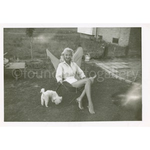 Beautiful Blonde Marilyn Monroe Look-A-Like Lounging in a Midcentury Modern B.K.F Butterfly Chair in the Yard with her Little Poodle Dog