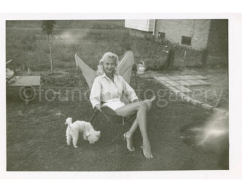 Beautiful Blonde Marilyn Monroe Look-A-Like Lounging in a Midcentury Modern B.K.F Butterfly Chair in the Yard with her Little Poodle Dog