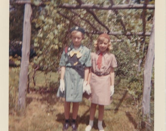 Hermanas, Junior Girl Scout y Brownie con guantes blancos bajo un cenador de uvas, foto vintage, instantánea en color