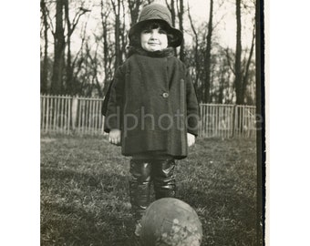 Awkward Girl standing in front of large ball of rock in field, winter coat and hat