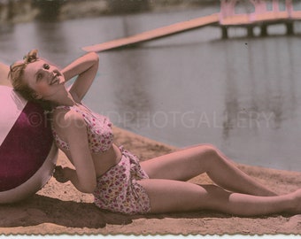 Classic Pin Up Girl in a Two Piece Halter Top Bathing Suit on the Beach Resting on A Big Pinwheel Ball, Vintage Photo, Color Postcard