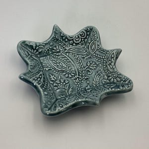 Puede incluir: Un plato de cerámica azul con un patrón de paisley. El plato tiene una forma única e irregular.