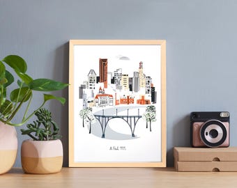 May include: A framed art print depicting a city skyline with a bridge. The artwork showcases buildings in shades of orange, white, and grey. The print is in a light wood frame, and the text "A Paul MN" is at the bottom.