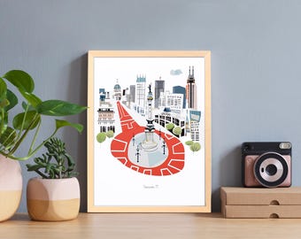 Puede incluir: Una impresión artística enmarcada que presenta una colorida ilustración de un horizonte urbano con un prominente monumento rojo y blanco en primer plano. La obra de arte se exhibe sobre una superficie de madera, junto a plantas en macetas y una cámara de estilo retro.