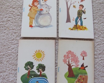 May include: Four illustrated cards depicting the four seasons. The first card shows a girl building a snowman in the winter. The second card shows a boy raking leaves in the fall. The third card shows two children swimming in a pond in the summer. The fourth card shows a bird perched on a branch of a tree in the spring.
