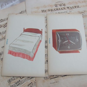May include: Two vintage illustrations on aged paper. One depicts a bed with a red headboard and a white comforter with a pink skirt. The other shows a red-framed clock with a black face. Background includes sheet music.