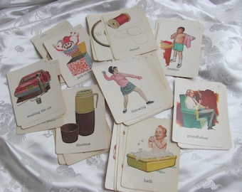 May include: A collection of vintage flashcards featuring illustrations and corresponding words. The cards depict various scenes and objects, including a car being washed, a thermos, a child in a bath, and a spool of thread. The cards are arranged on a white, patterned surface.