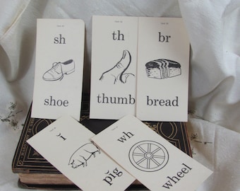 Op de afbeelding: Zes witte kaarten met zwarte illustraties en tekst. De kaarten tonen een schoen, een duim, brood, een varken, een wiel en de letter 'I'. De kaarten zijn gelabeld met de klanken 'sh', 'th', 'br', 'wh', 'p' en 'i'.