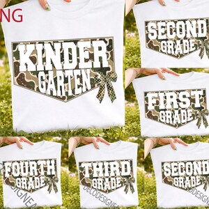 May include: A white t-shirt featuring a baseball home plate graphic with a camouflage pattern and a green polka dot bow. The text reads KINDER GARTEN, FIRST GRADE, SECOND GRADE, THIRD GRADE, or FOURTH GRADE in bold white letters across the center.