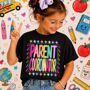May include: A black t-shirt featuring the text PARENT COORDINATOR in colorful, bold, multi-colored letters. The text is framed by a border of small, multi-colored stars and decorative squiggles, creating a vibrant and clear graphic design.