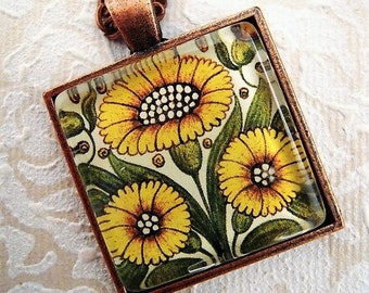 May include: A copper-toned necklace featuring a square pendant with a floral design. The pendant showcases yellow sunflowers with green leaves against a cream background. The necklace has a matching copper chain.