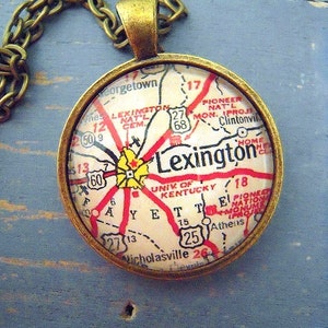 May include: A round pendant necklace with a map of Lexington, Kentucky. The pendant has a bronze-colored frame and chain. The map features red roads and the city name. The necklace is a unique accessory.