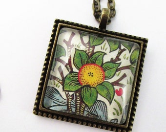 May include: Square pendant necklace with a floral design. The pendant has a bronze-colored frame with a beaded edge. The floral design features a yellow flower with green leaves and a red center, set against a cream background.