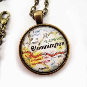 May include: A round pendant necklace with a map of Bloomington, Indiana, USA. The pendant has a bronze-colored frame and chain. The map includes the text "Bloomington", "Indiana Univ.", and "Handy".