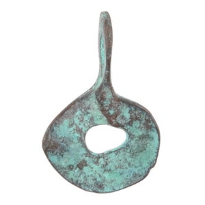 May include: A copper pendant with a unique, abstract design. The pendant has a hole in the center and a loop at the top for hanging. The copper has a green patina.