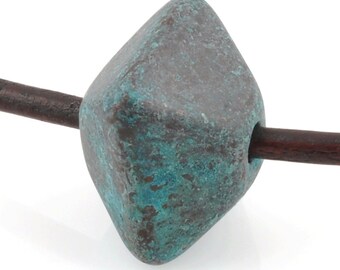 May include: A dark green and brown ceramic bead with a diamond shape. The bead is threaded on a brown leather cord.