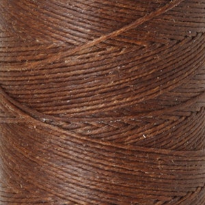May include: Close-up of a spool of brown waxed thread. The thread is tightly wound and has a smooth, polished finish.