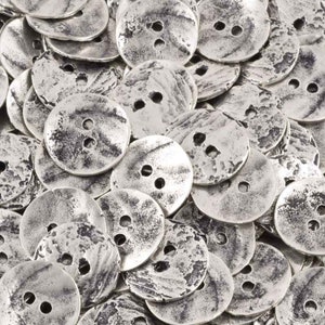 May include: A close-up of a pile of silver-toned metal buttons with a distressed finish. The buttons are round and have two holes each.