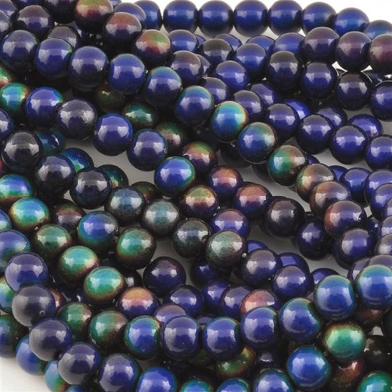 May include: Close-up of a collection of iridescent beads. The beads are a deep blue color with hints of green, purple, and bronze. The beads are round and appear to be strung together, suggesting they are for jewelry making or crafting.