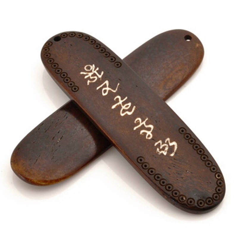K&ouml;nnte beinhalten: Zwei braune, ovale Holzgegenst&auml;nde mit einem dekorativen Rand aus kleinen Kreisen. Der obere Gegenstand tr&auml;gt eine silberne Inschrift in koreanischen Schriftzeichen.
