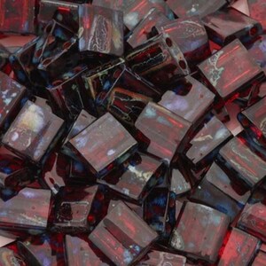May include: A collection of square, dark red beads with a glossy finish. The beads have a rectangular shape with a hole running through the center. The beads have a marbled appearance with hints of blue and black.