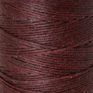 May include: Close-up of a spool of dark burgundy waxed linen thread. The thread is tightly wound, showing the texture and individual strands. Ideal for crafting, this thread offers a rich color and durable construction for various projects.