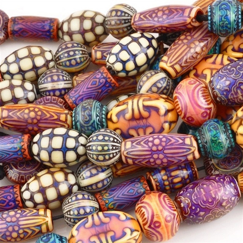 May include: A close-up of a collection of decorative beads in various shapes and sizes. The beads are in shades of orange, purple, blue, and cream, with intricate patterns. Some are oval, others round or cylindrical, creating a visually interesting assortment.